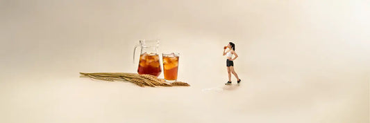 A glass of cold mugicha barley tea beside roasted barley grains, illustrating the drink's natural, grain-based ingredients.