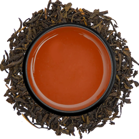 A cup of pink Nadeshiko fermented tea seen from above, ringed by its dried leaves on a white background