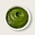 A top-down view of a thick, vibrant green puree, likely avocado or pumpkin puree, swirled in a white ceramic bowl against a light gray background.